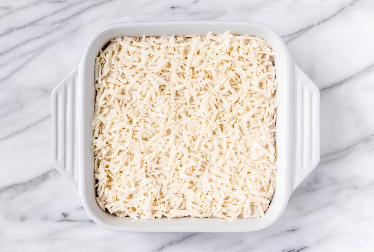Shredded cheese on top of a white, square casserole dish