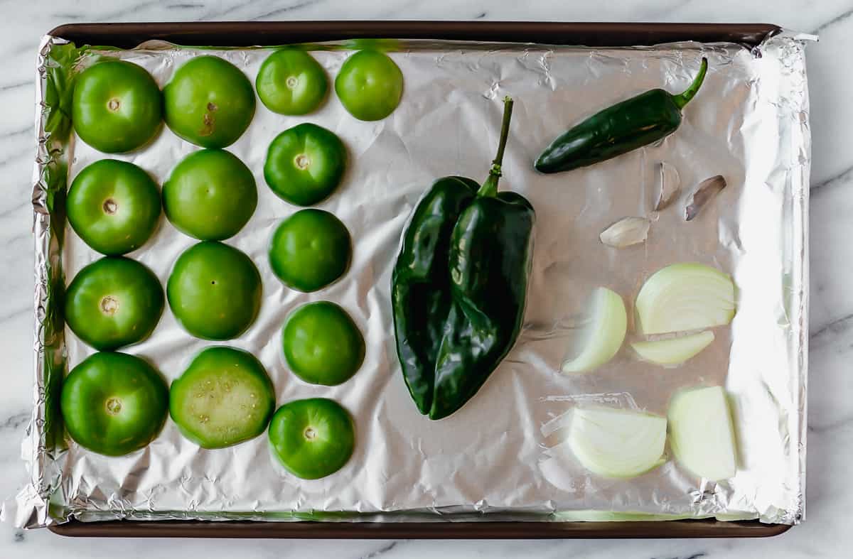 Tomatillos, poblano, jalapeno, onion and garlic on an aluminum foil covered sheet pan