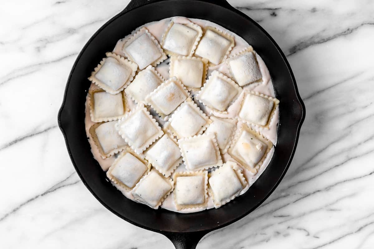 Ravioli over alfredo sauce in a cast iron skillet on a marble backdrop