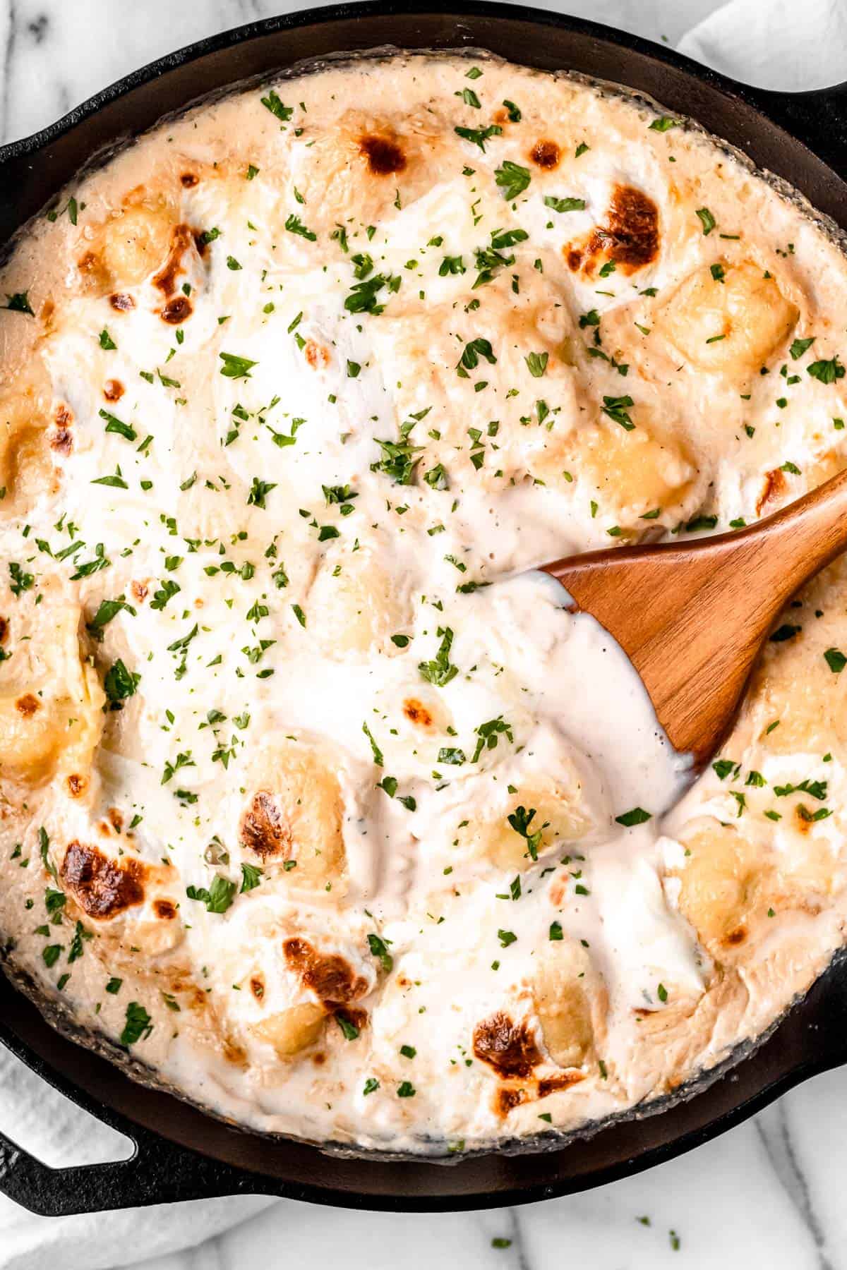 close up of Ravioli Alfredo casserole in a cast iron skillet with a wood server in it