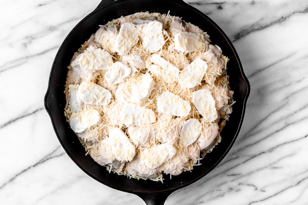 2 layers of ravioli with alfredo sauce, mozzarella cheese and parmesan cheese in a cast iron skillet