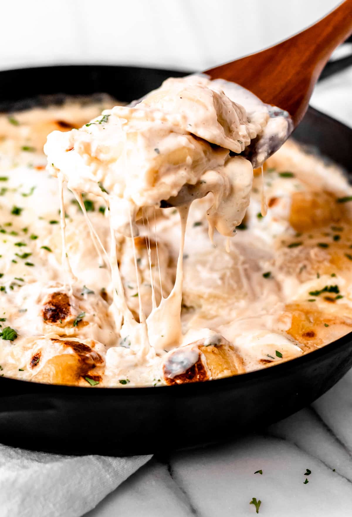 Baked ravioli casserole being lifted up with a wood sever and cheese pulls coming down off it