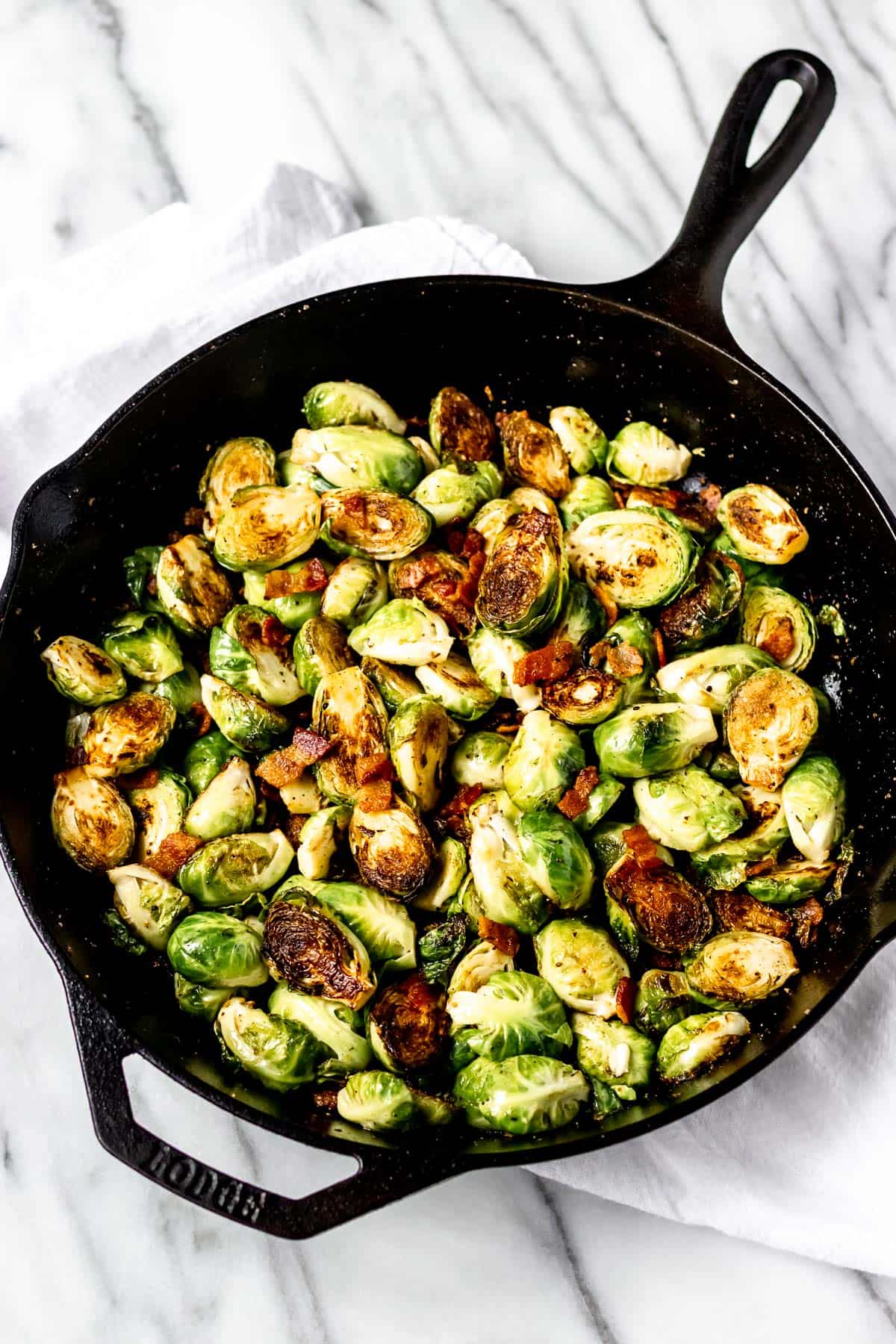 Brussels sprouts with bacon in a cast iron skillet on a marble backdrop