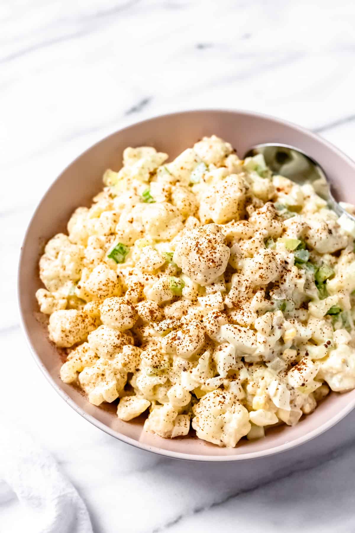 Cauliflower potato salad in a pink bowl with a spoon in it over a marble background