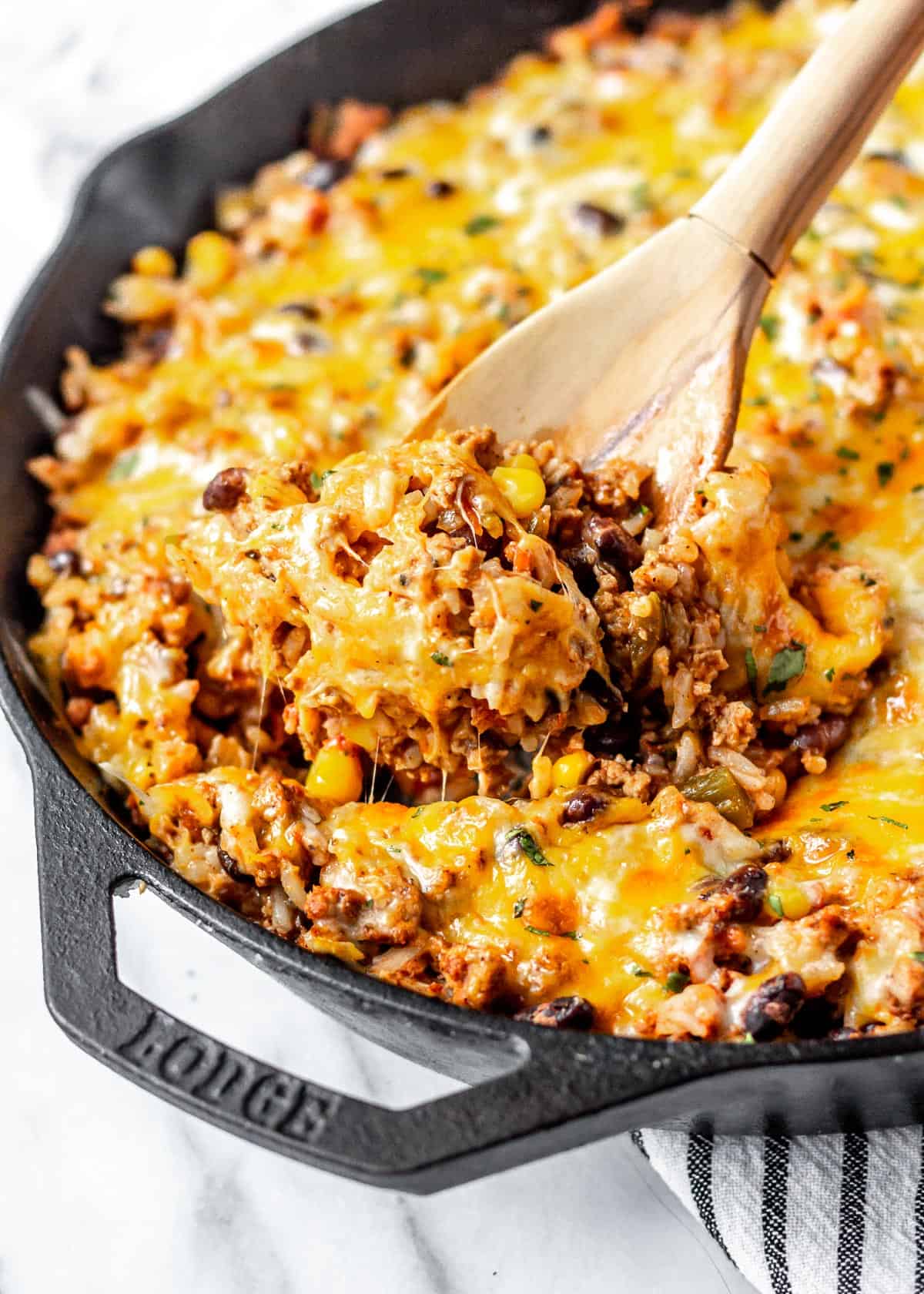 Close up of a cheesy taco skillet in a cast iron pan with a wood spoon lifting some up