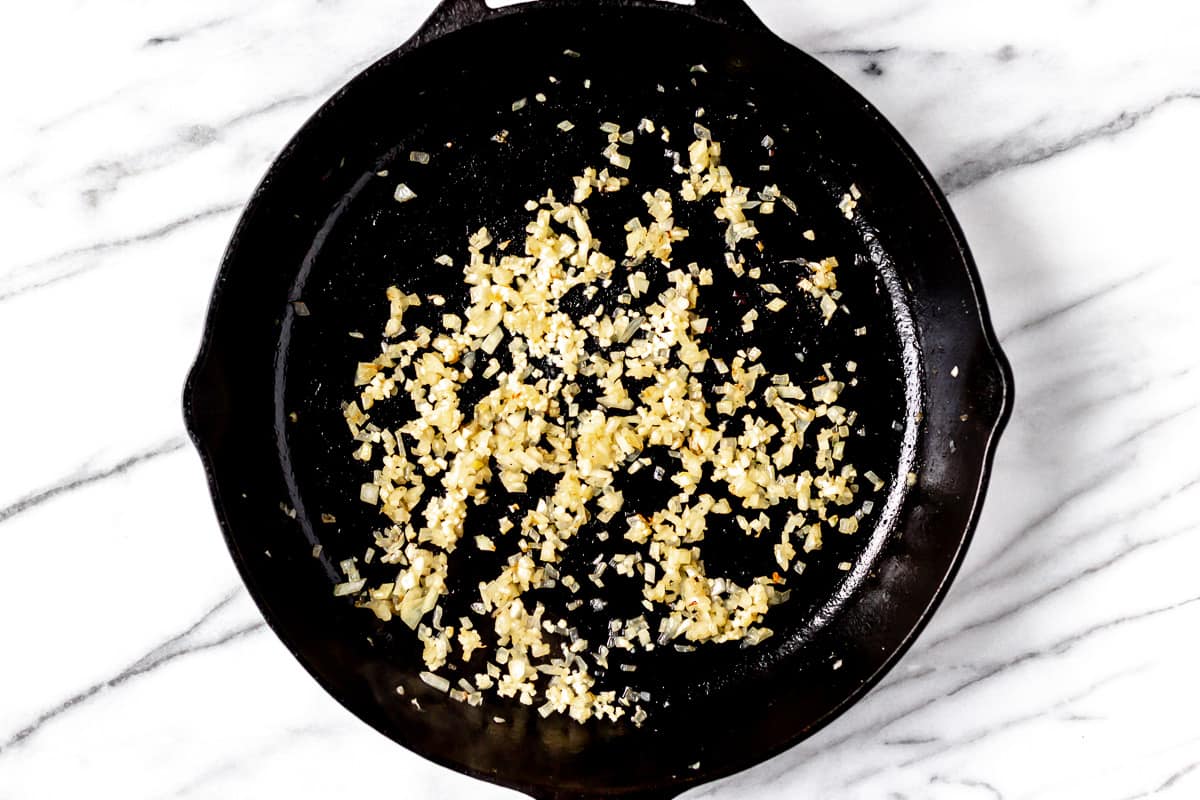 Onion and garlic cooking in a black cast iron skillet