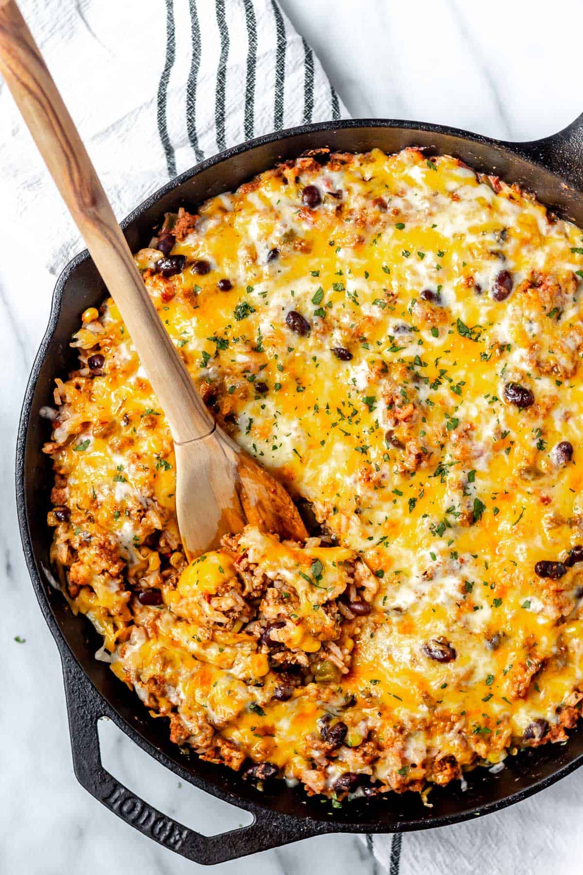 Overhead of a cheesy taco skillet in a cast iron pan with a wood spoon pushing some up