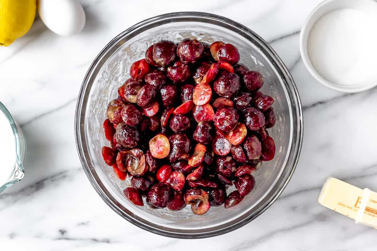 Cherries, sugar, cinnamon and flour combined in a glass bowl with other ingredients around it