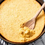 Corn souffle being scooped up with a wood spoon in a cast iron skillet