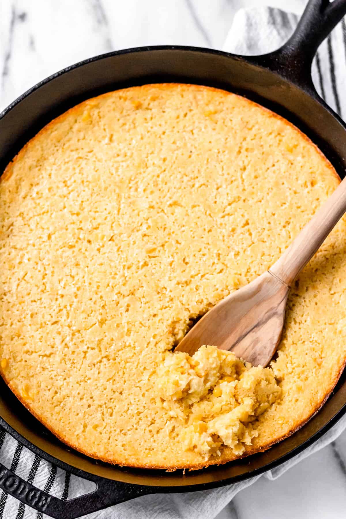 Corn soufflé being scooped up with a wood spoon in a cast iron skillet