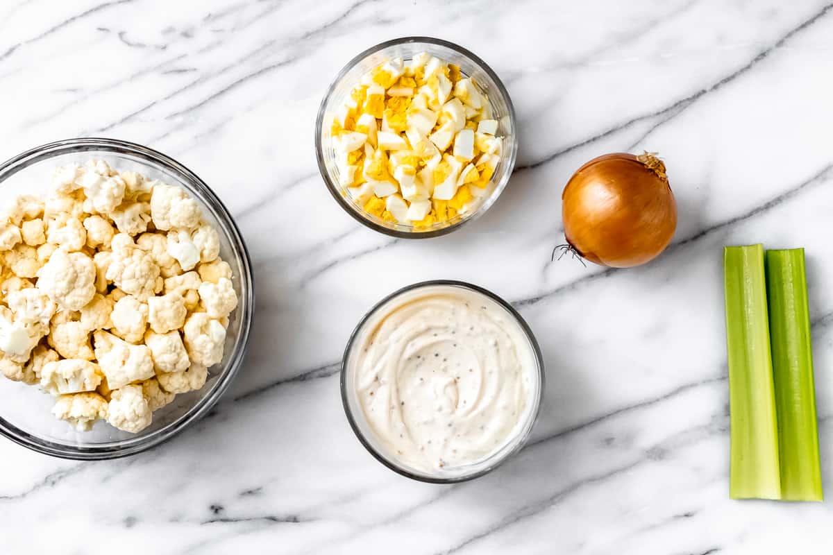 Cauliflower potato salad dressing in a small bowl with other ingredients around it