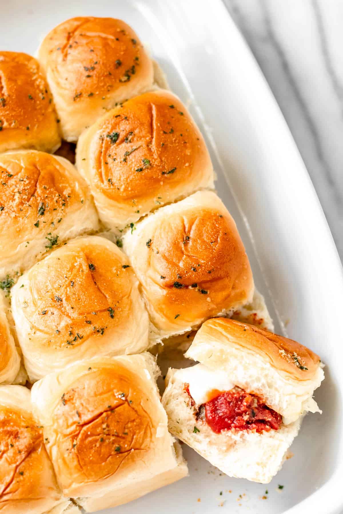 Meatball sliders in a white baking dish with one turned sideways to show what's inside