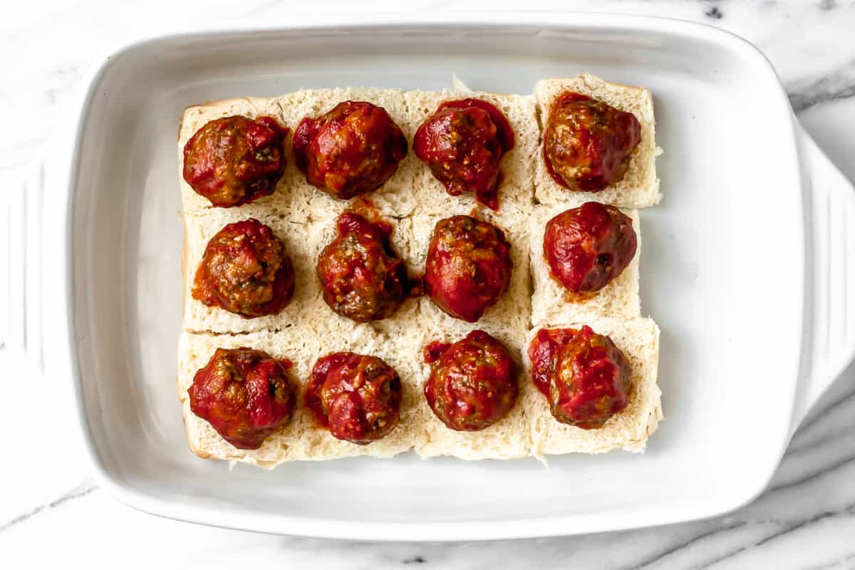 Slider rolls in a baking dish with a sauced meatball on each one