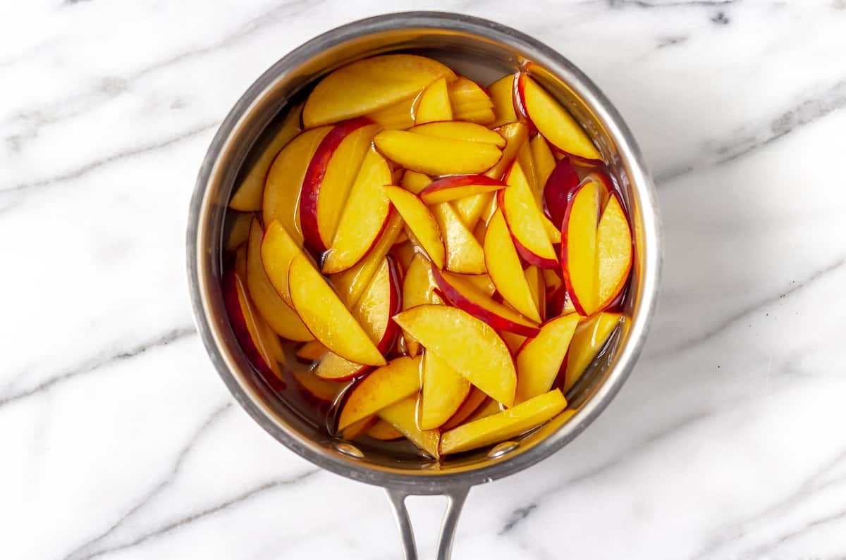 Sliced peaches in a sauce pot on a marble backdrop