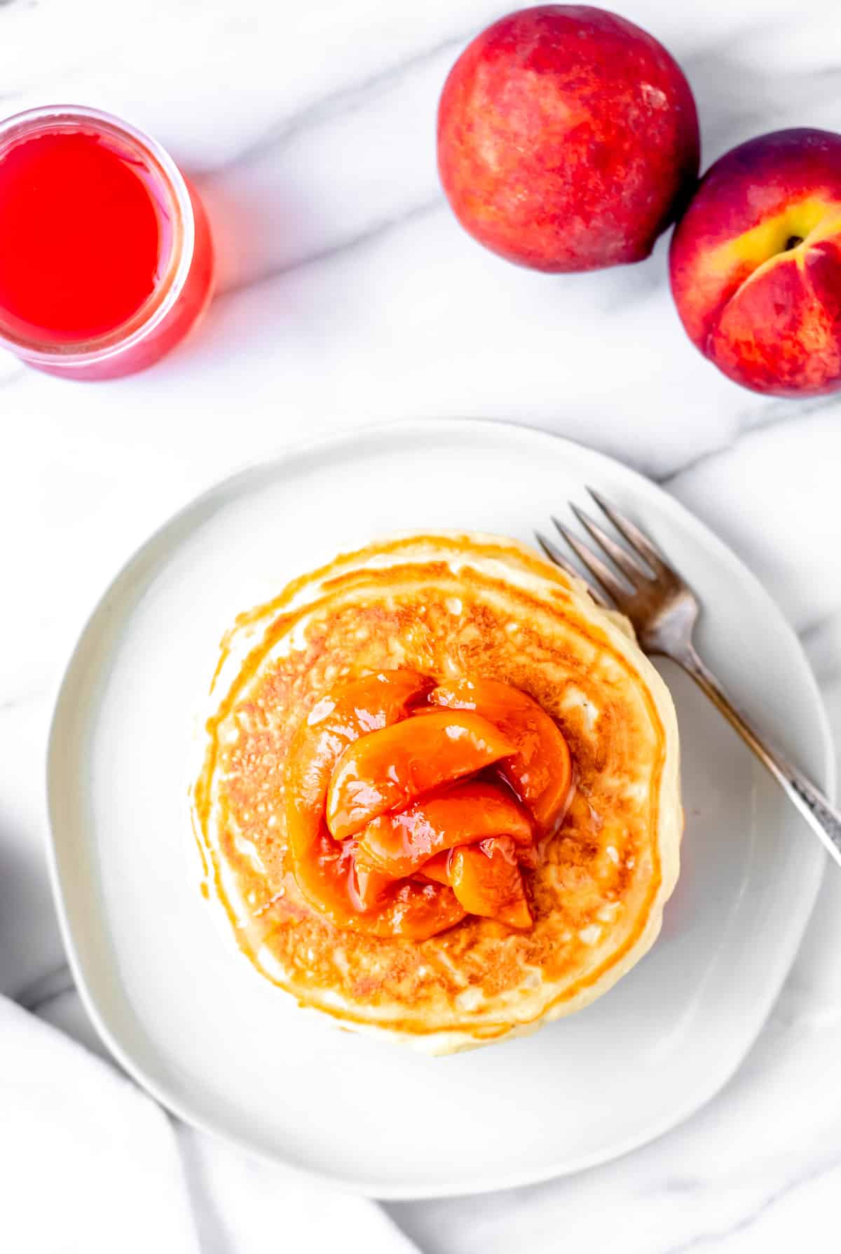 pancakes with peaches on to and a jar of peach syrup and whole peaches in the. background