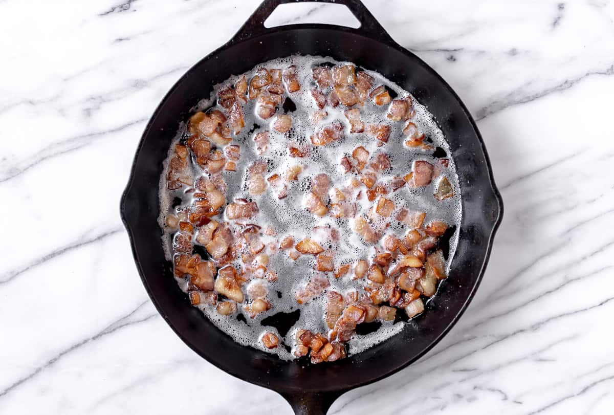 Diced bacon cooking in a cast iron skillet