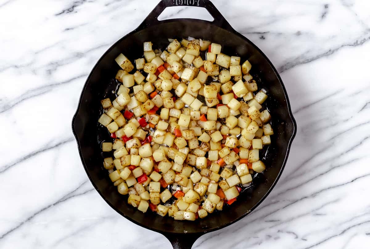 Diced potatoes, peppers and onion cooking in a cast iron skillet