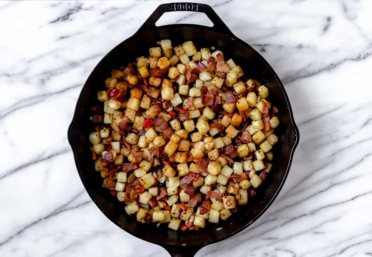 Diced potatoes, bacon, red pepper and onions in a cast iron skillet