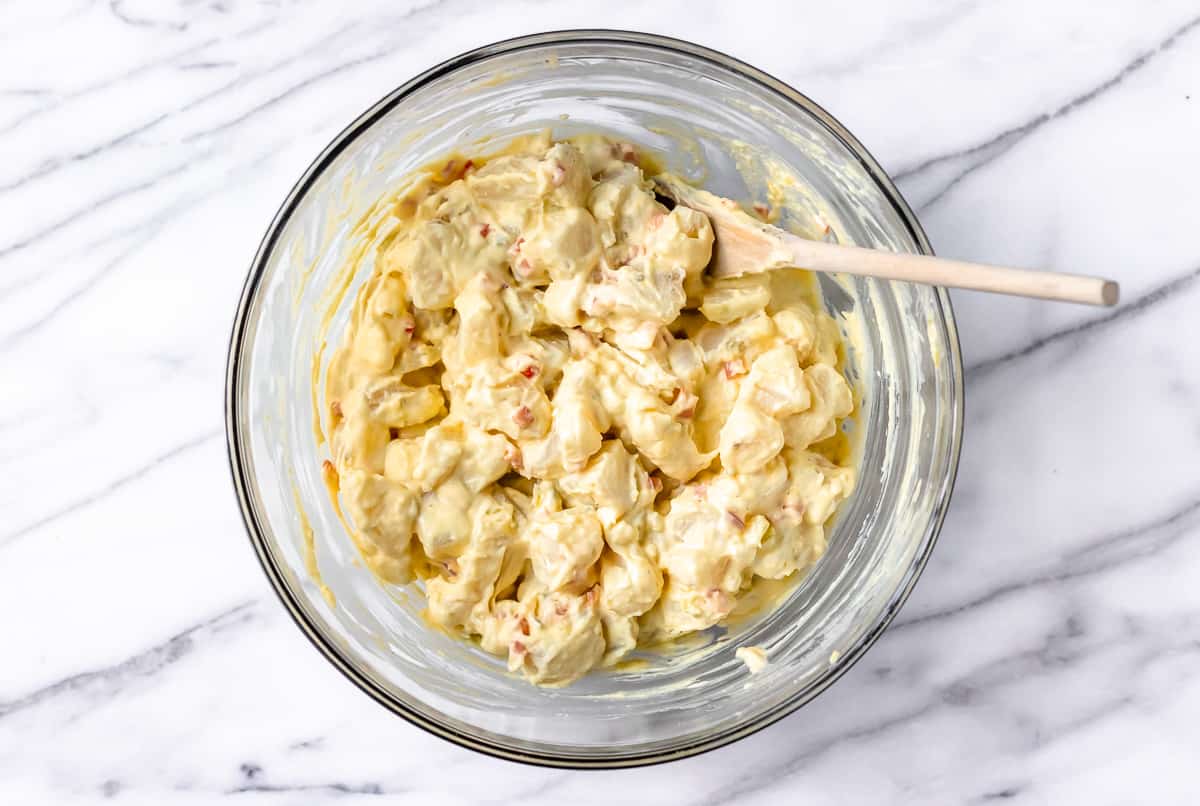 Potato salad vegetables and dressing combined in a large glass bowl over a marble background