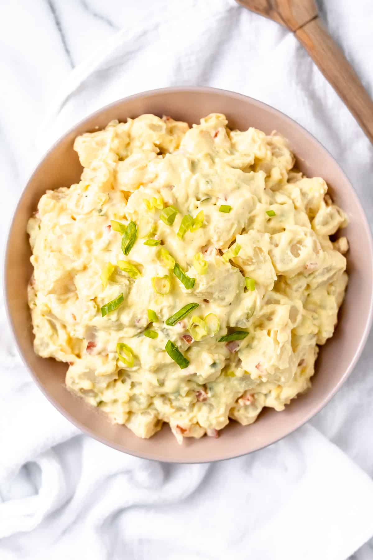 Overhead of amish potato salad on a marble background with a white dish towel and wood spoon
