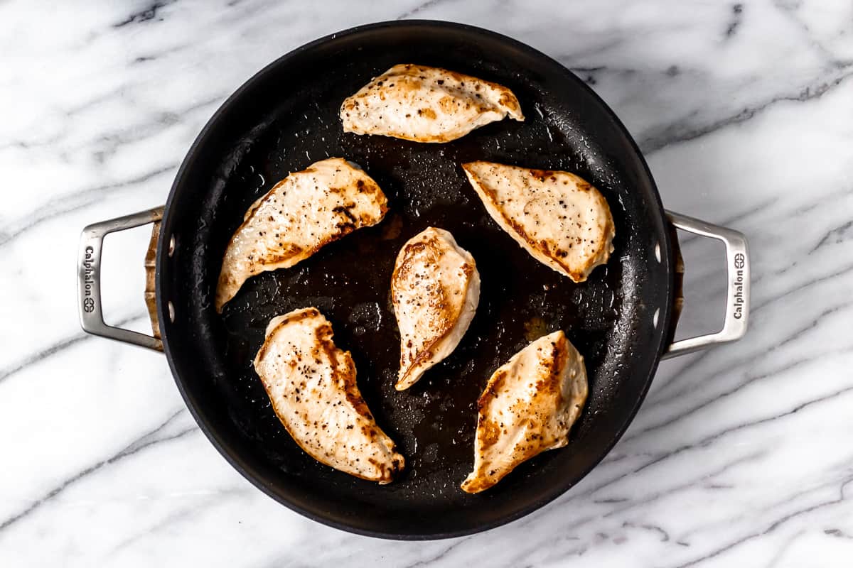 6 pieces of chicken in a black skillet over a marble background