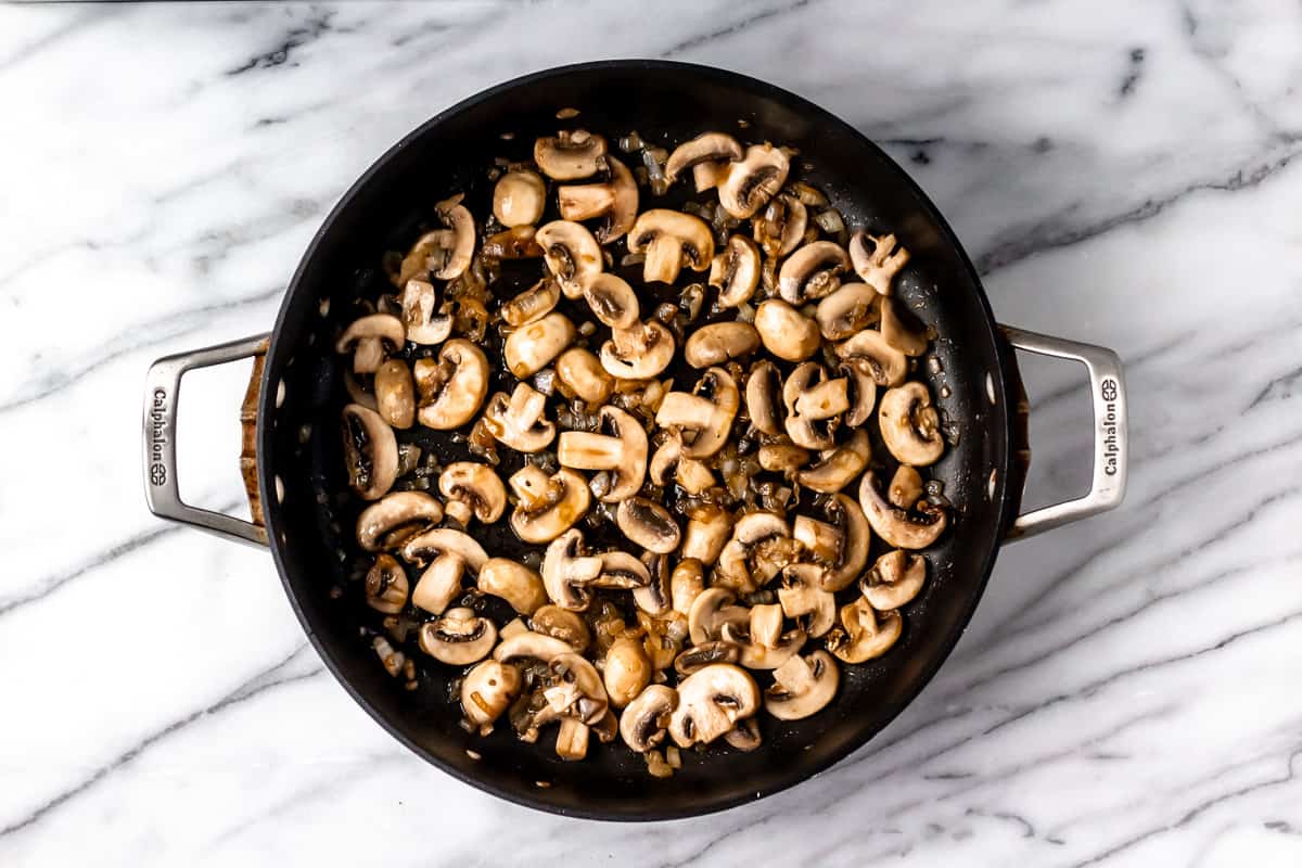 Mushrooms and onions in a black skillet over a marble background