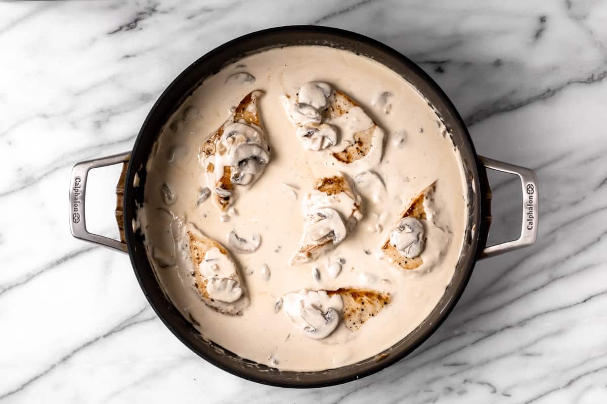 Chicken in a cream sauce in a black skillet over a marble background