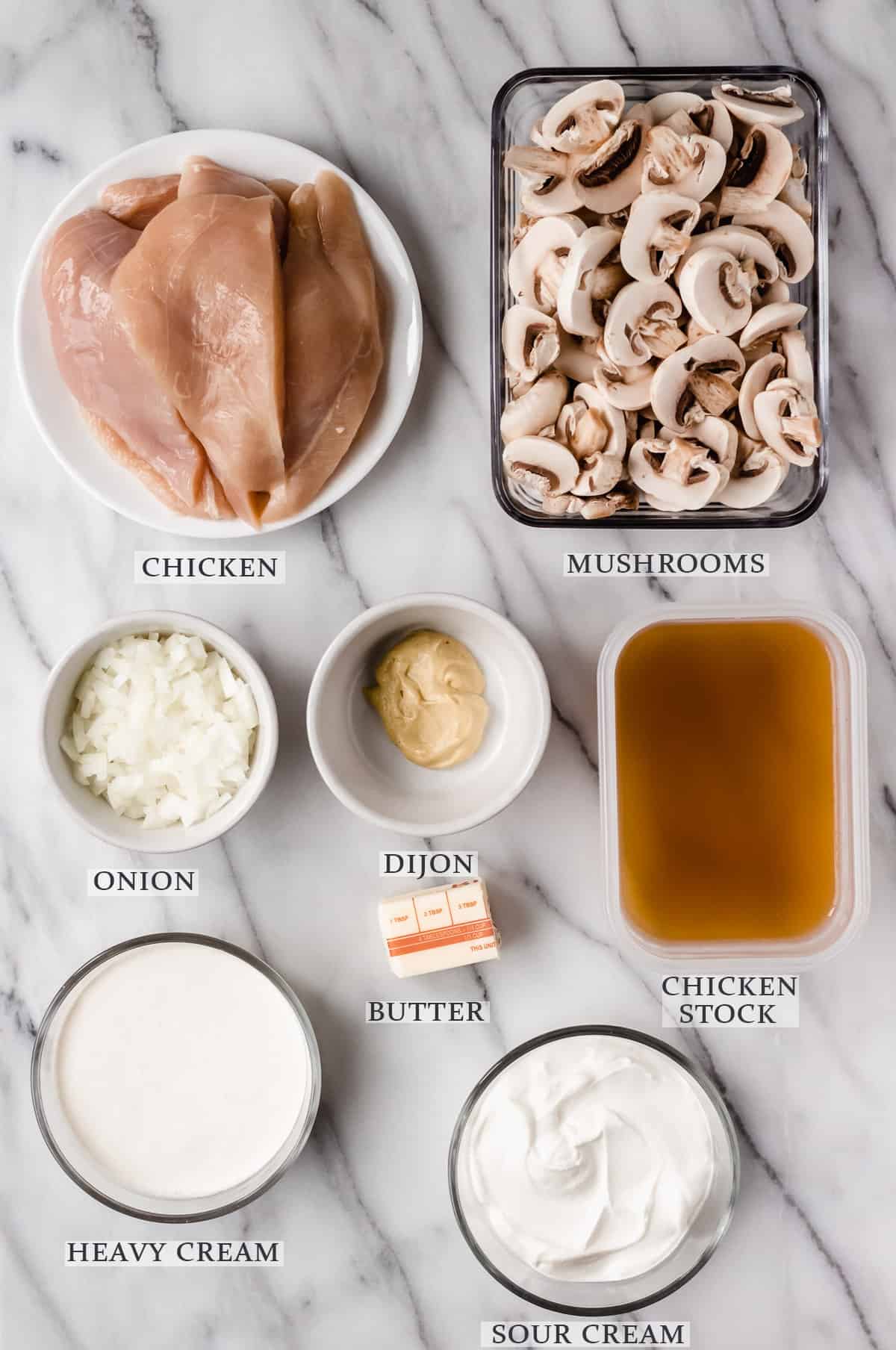 Ingredients needed to make chicken stroganoff on a marble background with labels