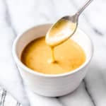 Close up of honey mustard drizzling off a spoon into a small white bowl