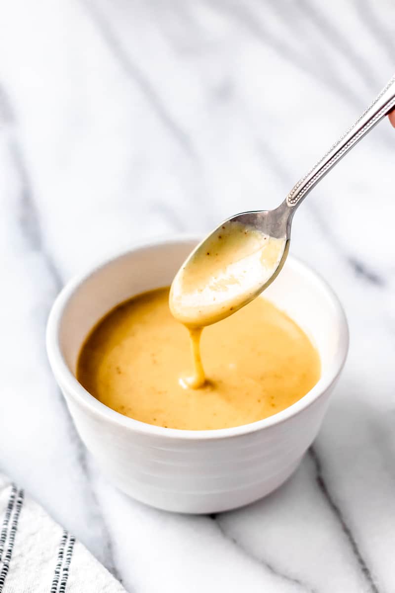 Honey mustard drizzling off a spoon into a small white bowl