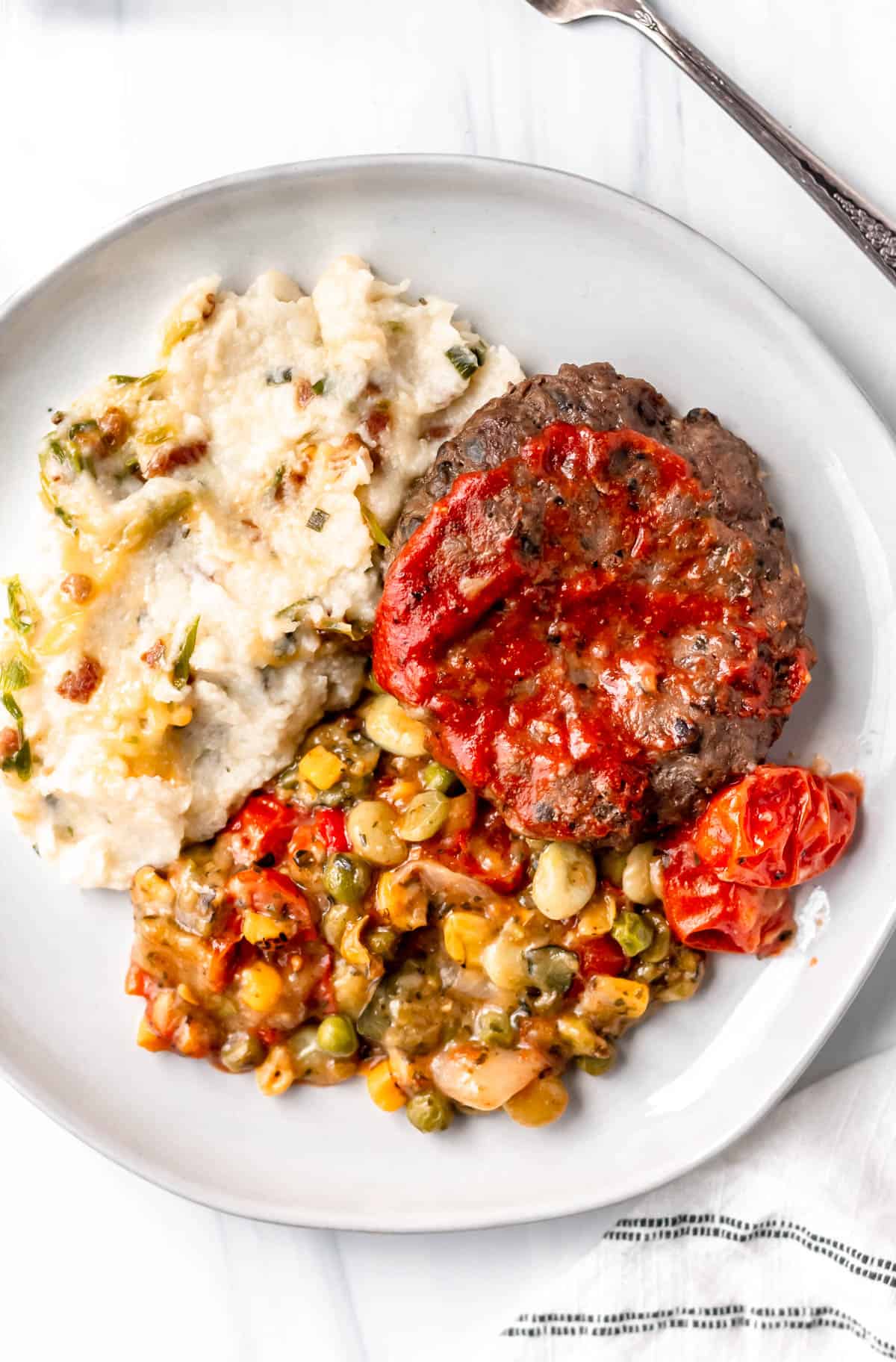 Freshly bunless bison burger, mashed potatoes and succotash on a white plate.