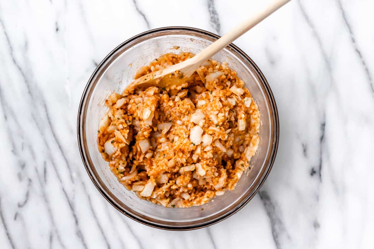 Cod cake batter in a glass bowl with a wood spoon over a marble background.