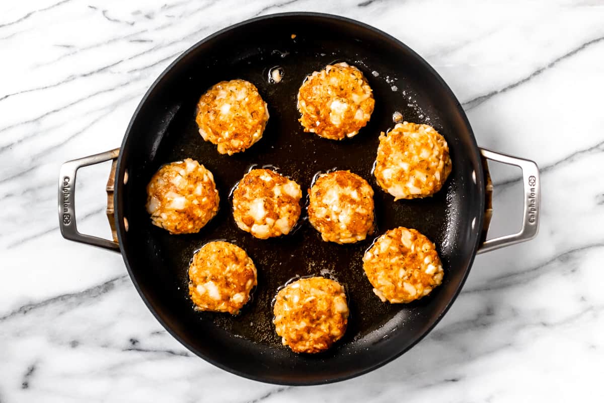 Overhead of cod cakes cooking in a black skillet.