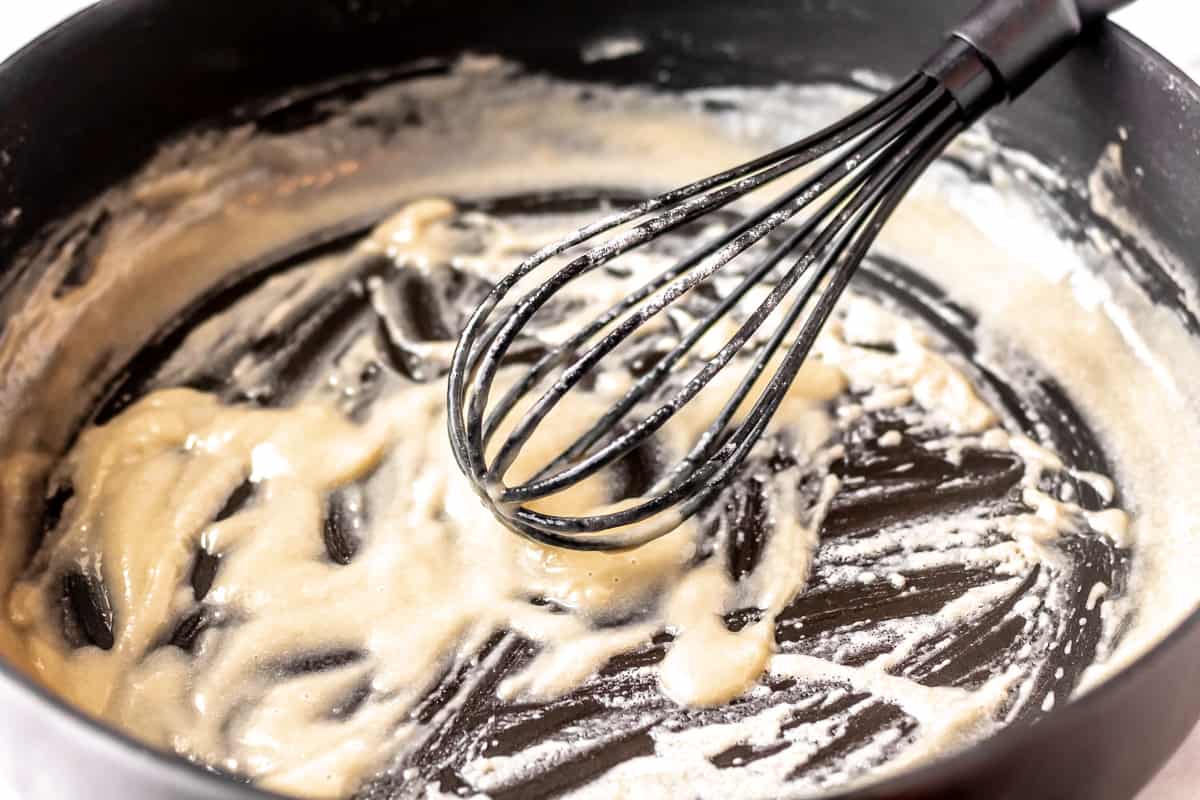 Butter, flour mixed together with a black whisk in a black skillet.
