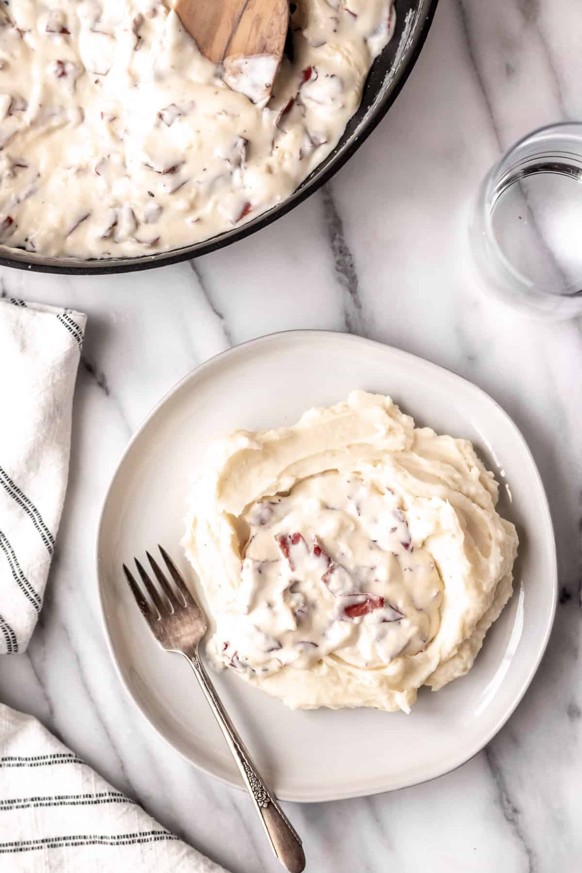 Overhead of creamed chipped beef on mashed potatoes with a fork, towel and skillet with a spoon in it over a marble backdrop.