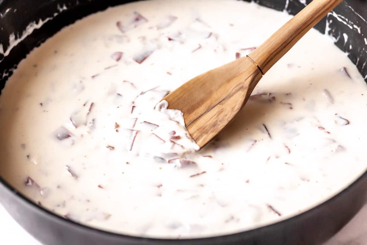 Bechamel sauce with dried beef and a back whisk in a black skillet.