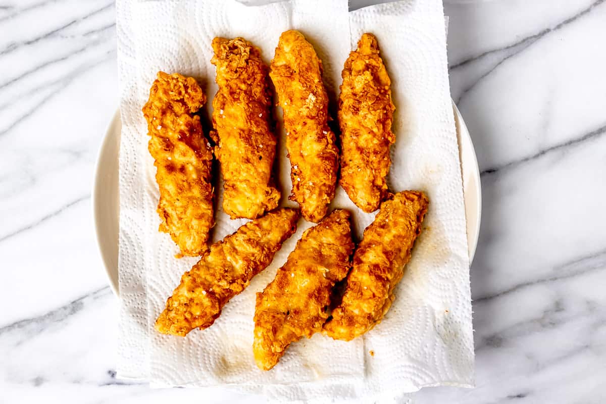 Fried chicken tenders on a paper-towel lined plate over a marble background.