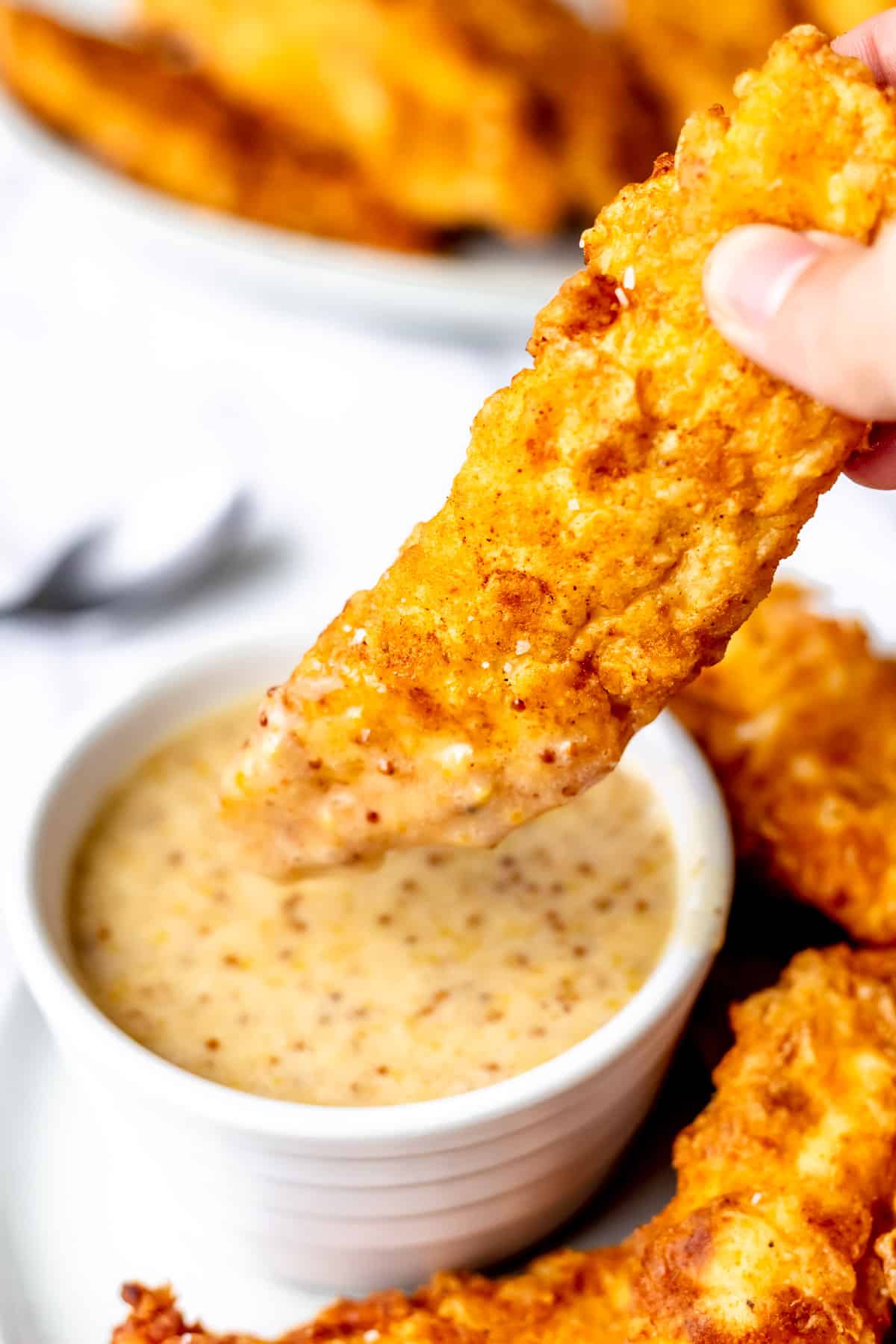 A fried chicken strip being dipped into a bowl of honey mustard.