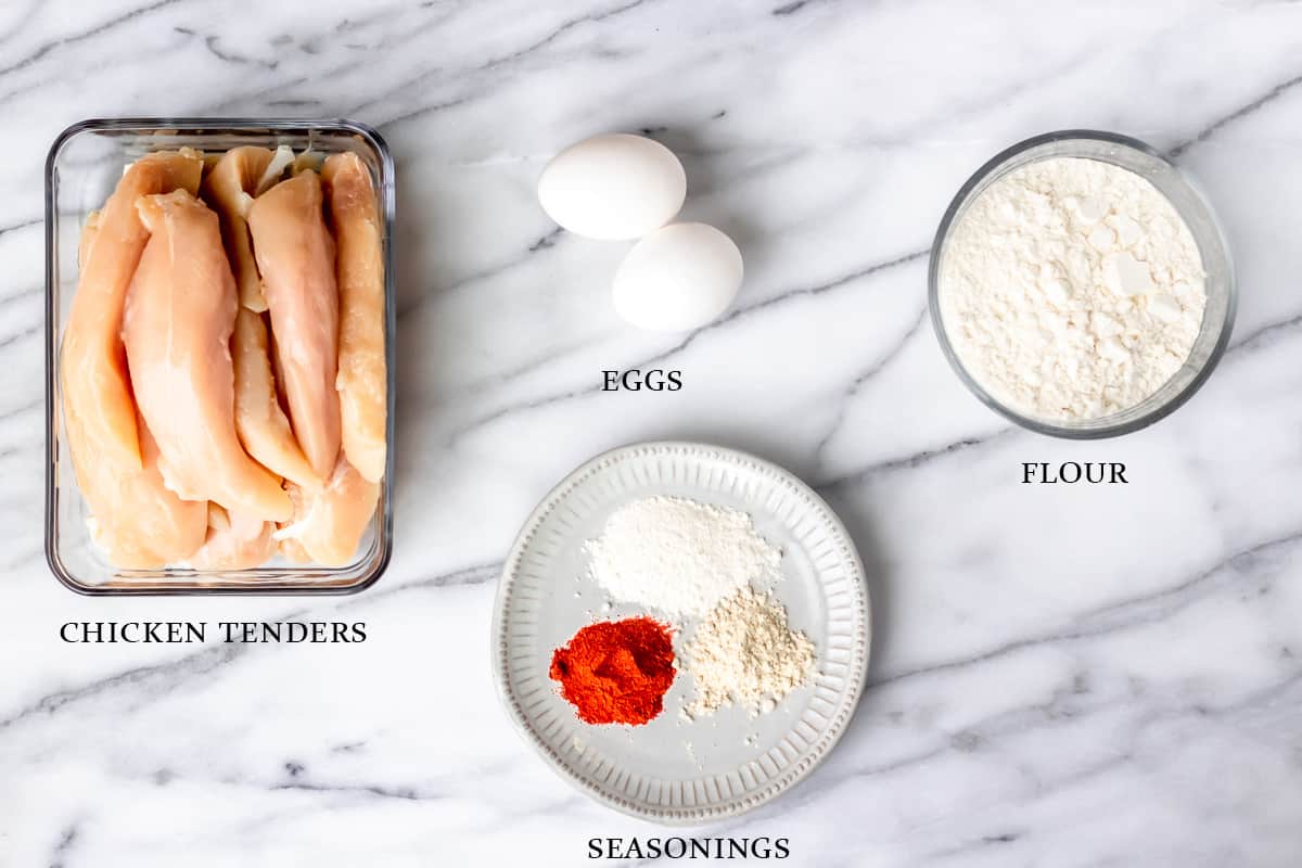 Ingredients needed to make fried chicken tenders on a marble background with text overlay.