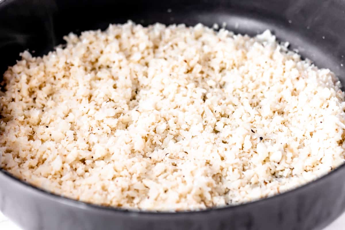 Cauliflower rice cooking in a black skillet