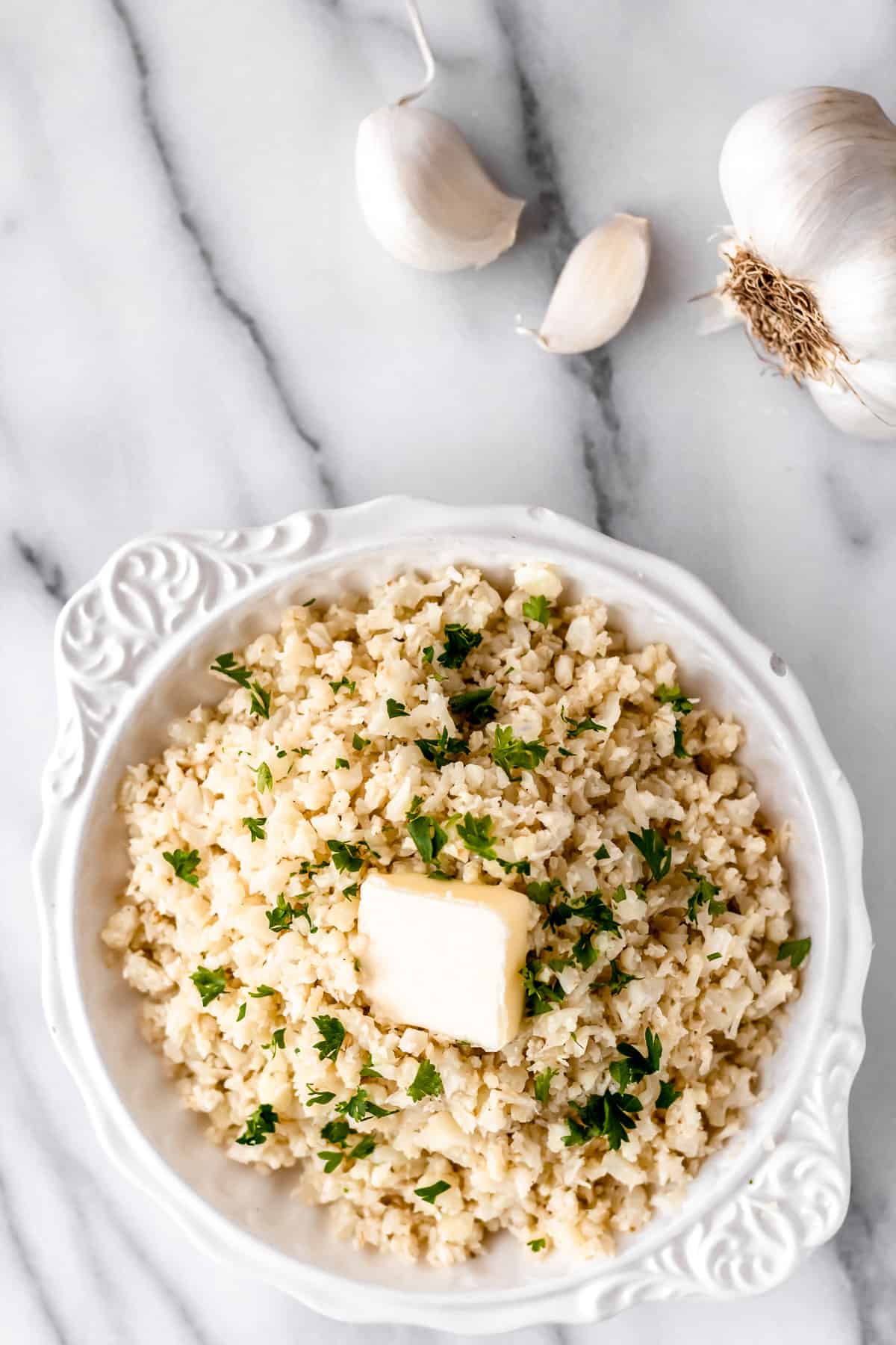 Overhead of garlic cauliflower rice in a white bowl with garlic cloves around it