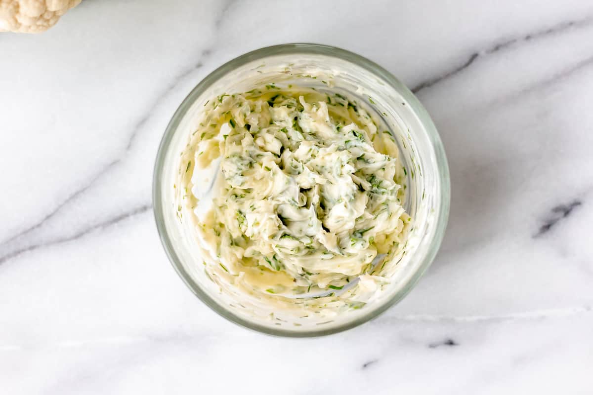 Garlic herb butter in a small glass bowl over a marble background.