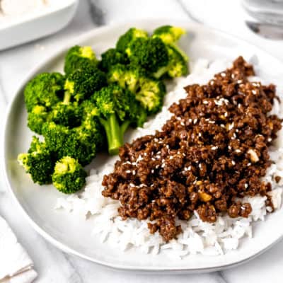 Close up of Mongolian ground beef on rice with broccoli in the background.