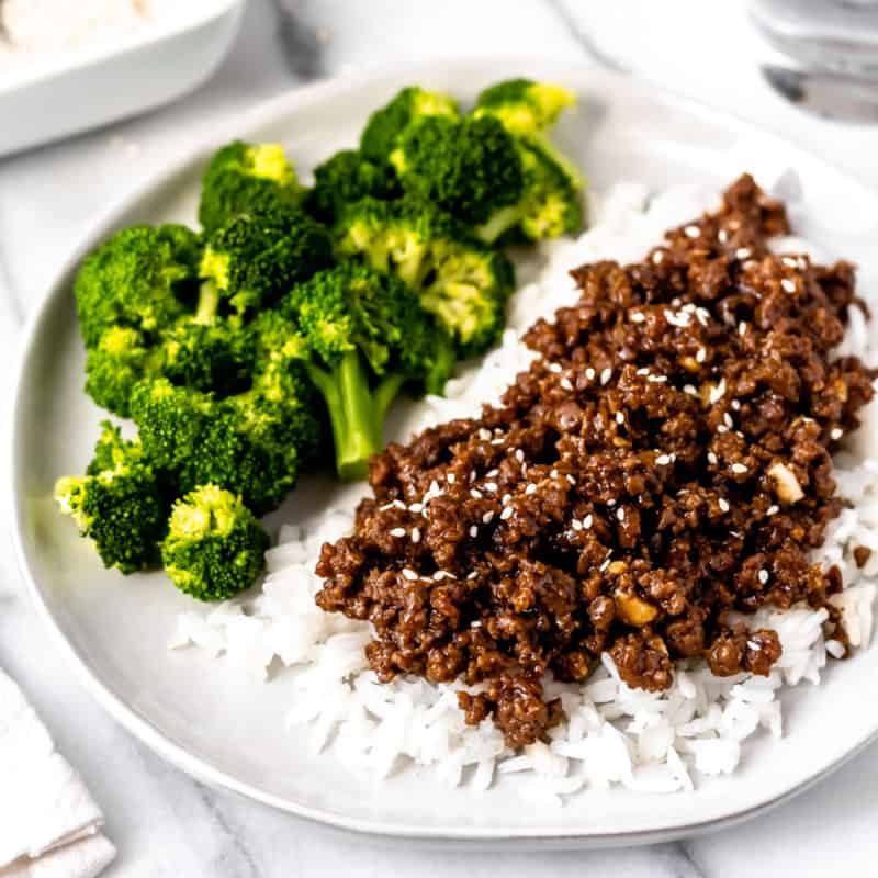 Close up of Mongolian ground beef on rice with broccoli in the background.