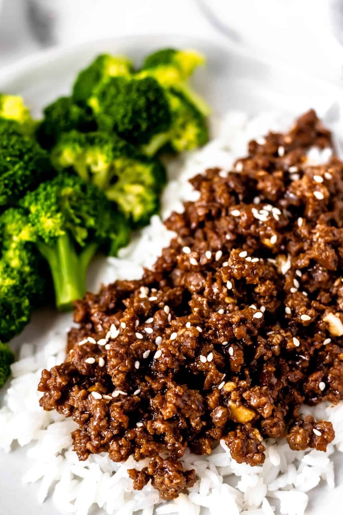 Close up of Mongolian ground beef on rice with broccoli in the background.