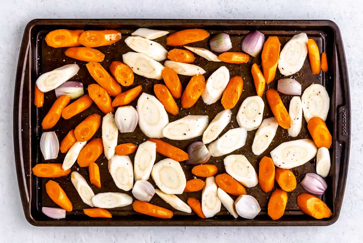 Raw carrots and parsnips slices spread out on a baking sheet.