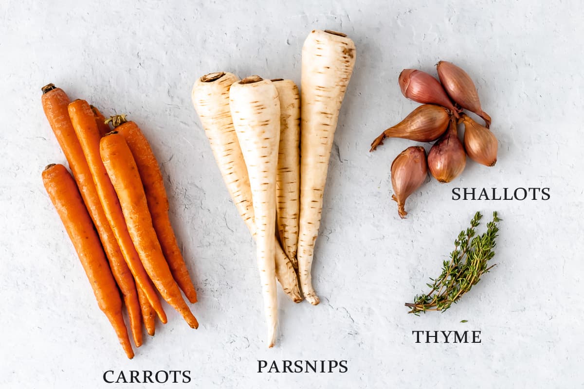 Ingredients to make roasted carrots and parsnips on a white background with text overlay.