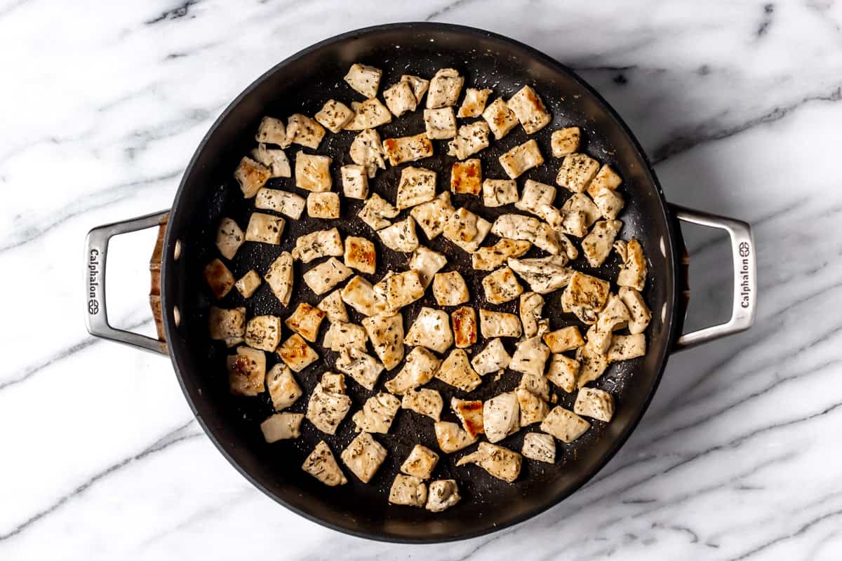 Chunks of chicken cooking in a black skillet.