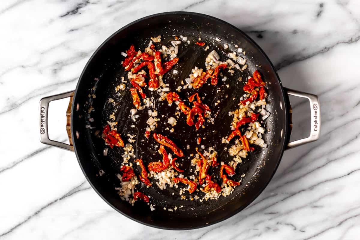 Garlic, shallot and sun-dried tomatoes cooking in a black skillet.