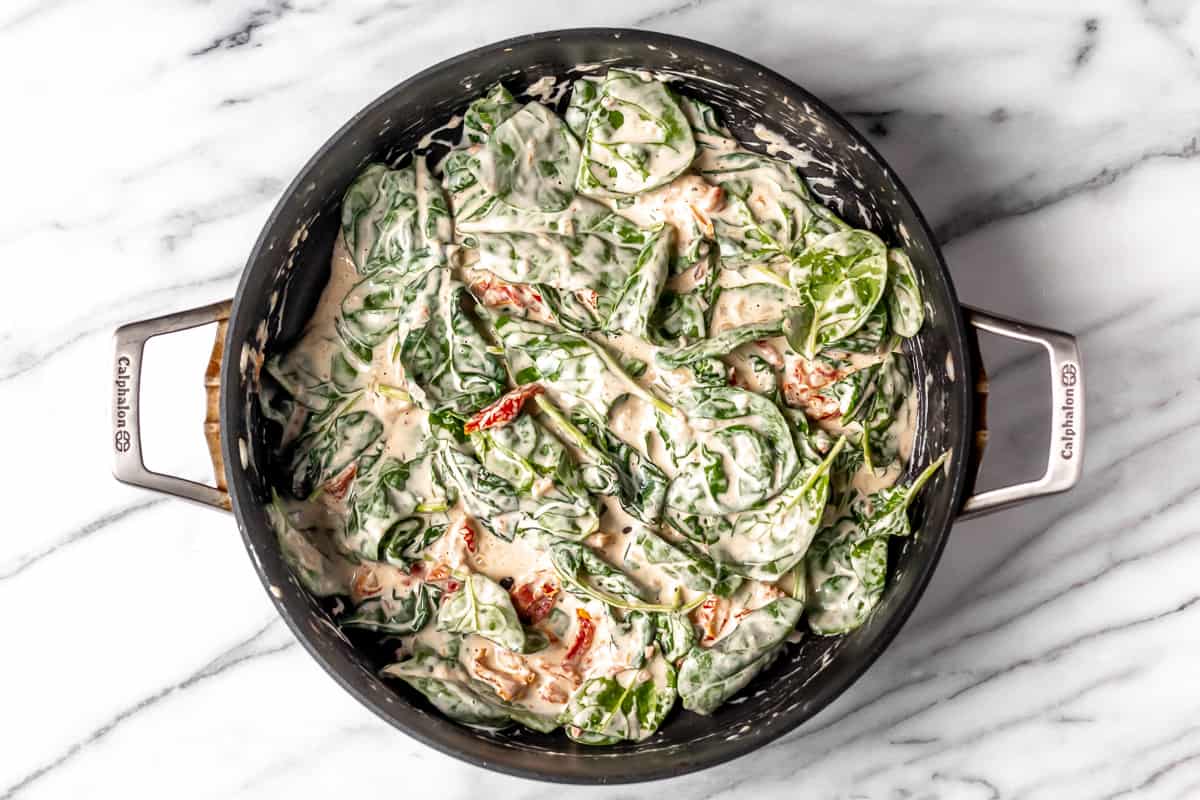 Spinach and sun-dried tomatoes in a cream sauce in a black skillet.